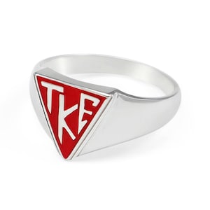 Puede incluir: Un anillo de plata con una parte superior triangular roja. El triángulo tiene letras blancas que dicen "TKE".