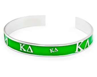 May include: A silver bangle bracelet with a green enamel band and white lettering that reads "KA".