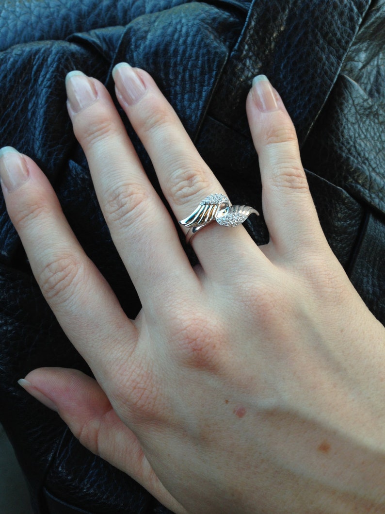 Puede incluir: Un anillo de plata con una piedra transparente engastada en forma de alas.