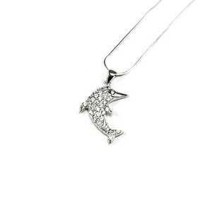 May include: A silver dolphin pendant necklace with clear cubic zirconia stones. The dolphin is facing to the right and has a detailed design.