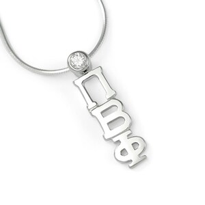 Puede incluir: Collar de plata con una pequeña piedra preciosa transparente y un colgante con las letras 'ПВФ' en una pila vertical.