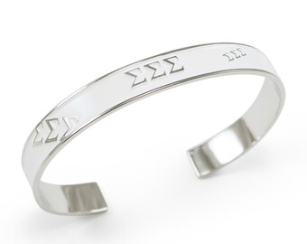 May include: A silver bangle bracelet with a white enamel band and the letters "ΣΣΣ" engraved on it.