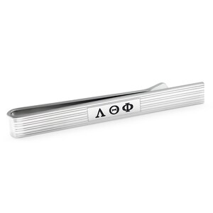 May include: Silver tie bar with a ridged surface and a rectangular black plaque with the letters "ΛΘΦ" engraved in white.