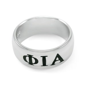 Könnte beinhalten: Ein silberner Ring mit den Buchstaben "ΦΙΑ" in Schwarz graviert.