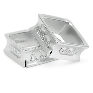 Può includere: Due anelli d'argento con bande quadrate. Gli anelli sono incisi con il numero romano 'MX' e l'anno '1909'.