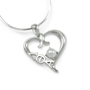 Puede incluir: Un collar de plata con un colgante en forma de corazón, una perla en el centro y las letras "AOA" inscritas en el colgante.