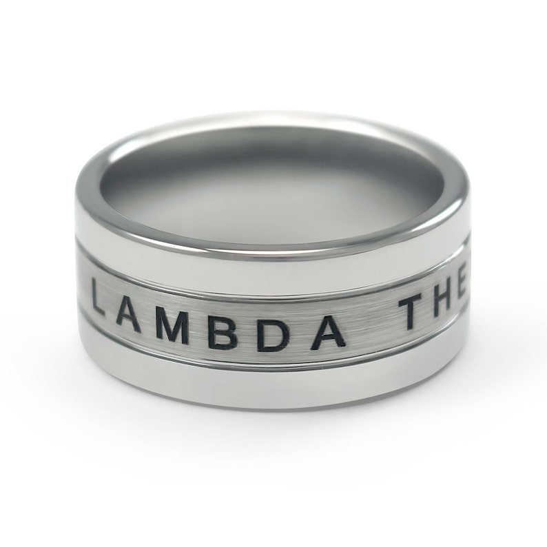 Puede incluir: Un anillo de plata con acabado cepillado y la palabra "LAMBDA" grabada en la banda.