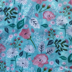 May include: Close-up of a floral fabric with a light blue background. The fabric features pink roses, white daisies, and green leaves. The pattern is a repeating design of flowers and foliage.