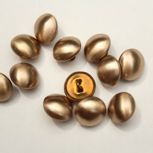 May include: A group of 10 gold-coloured buttons, some with a shiny finish and others with a matte finish. One button has a gold-coloured letter "B" on it.