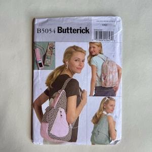 May include: A Butterick sewing pattern envelope, B5054, featuring images of a woman wearing a backpack. The backpack designs include pink, black and white polka dots, and floral patterns. The envelope is light-colored with text and images.
