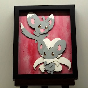 Puede incluir: Una pieza de arte en papel enmarcada con dos criaturas grises y blancas de estilo caricatura con orejas grandes y detalles en rosa. El fondo es un lavado de estilo acuarela en rosa y rojo. El marco es negro.