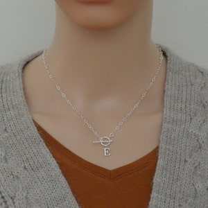 May include: A silver chain necklace with a toggle clasp and a small letter 'E' charm.