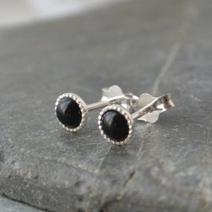 May include: A pair of silver stud earrings with black onyx stones. The stones are set in a silver bezel with a beaded edge.
