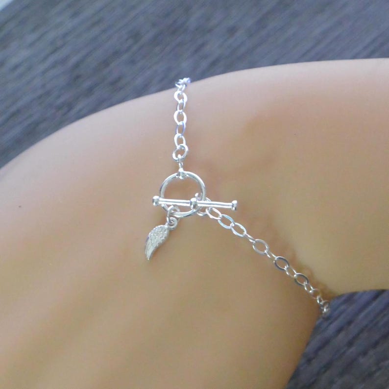 Pu&ograve; includere: Un bracciale d'argento con chiusura a toggle e un piccolo ciondolo a forma di piuma. Il bracciale &egrave; composto da sottili maglie a catena.