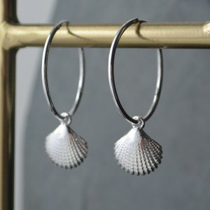 May include: Silver hoop earrings with a small seashell charm hanging from each hoop.