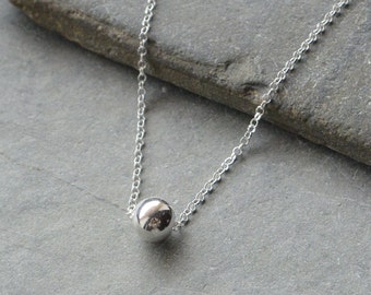 May include: A silver chain necklace with a single, round silver bead pendant.