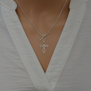 May include: A silver necklace with a toggle clasp and a delicate, intertwined cross pendant.