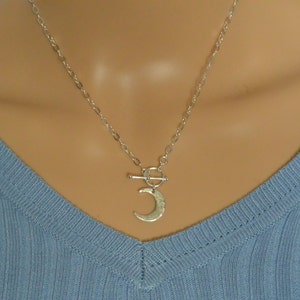 May include: A silver chain necklace with a toggle clasp and a hammered crescent moon pendant.