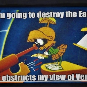 May include: A cartoon image of Marvin the Martian, a green alien with a helmet, holding a weapon and saying "I'm going to destroy the Earth. It obstructs my view of Venus."