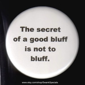 May include: White button with black text that reads "The secret of a good bluff is not to bluff."