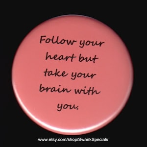 May include: A pink round button with the text "Follow your heart but take your brain with you." printed in black.