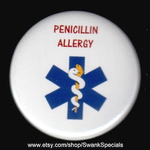 Pode incluir: Botão branco com o texto "Penicillin Allergy" em letras vermelhas. Um símbolo azul de estrela da vida com uma cobra amarela está no centro do botão.