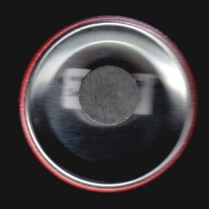 May include: Close-up of the back of a round button with a red border. The button has a silver backing with a black circle in the center.