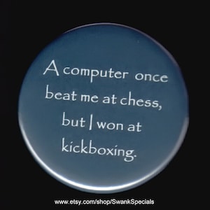 May include: A blue round button with white text that reads "A computer once beat me at chess, but I won at kickboxing." The text is centered on the button. The button has a white border.