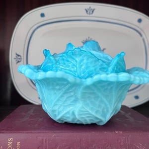 May include: A bright turquoise blue milk glass bowl shaped like a cabbage head with a matching lid. The bowl features detailed embossed leaf textures and scalloped edges, creating a realistic vegetable appearance in a vibrant, semi-translucent glass.
