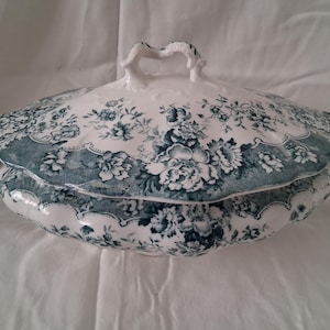 May include: A white and teal floral patterned serving dish with a lid. The dish has a scalloped edge and a handle on the lid. The floral pattern is a detailed design of flowers and leaves. The dish is likely made of ceramic.