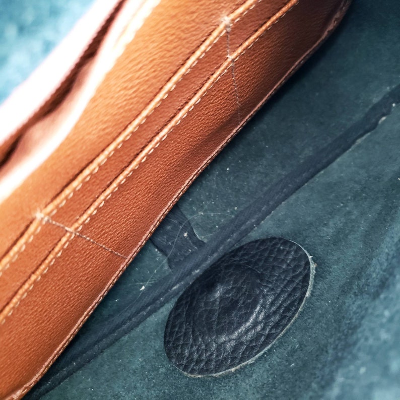 May include: Close-up of the inside of a brown leather bag with a black leather patch. The bag has a stitched design and a soft, textured lining.