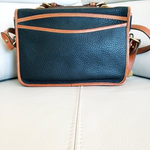 May include: A black leather satchel with brown trim and a gold buckle. The bag has a flap closure and a shoulder strap.