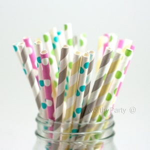 May include: A close-up of a glass jar filled with colorful paper straws. The straws have different patterns, including polka dots, stripes, and a teal blue color. The straws are arranged in a random order, creating a visually appealing display.