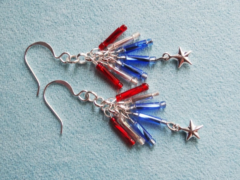 May include: A pair of silver earrings with red, white, and blue glass beads and silver star charms. The earrings are designed to look like fireworks.