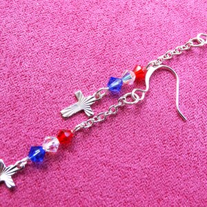 May include: Silver dangle earrings with red, white, and blue crystal beads and silver cross charms.