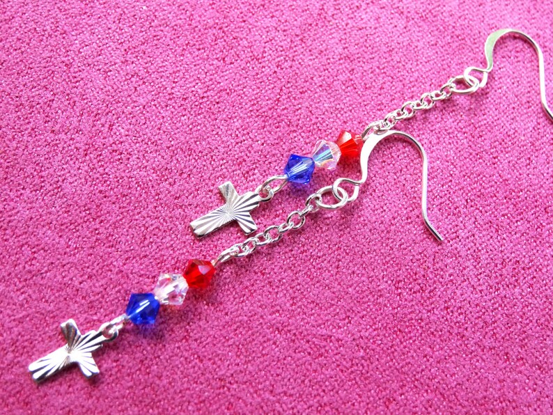 May include: Silver dangle earrings with red, white, and blue crystal beads and silver cross charms.