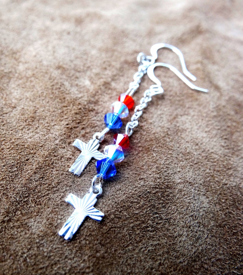 May include: Silver dangle earrings with red, white, and blue crystal beads and silver cross charms.