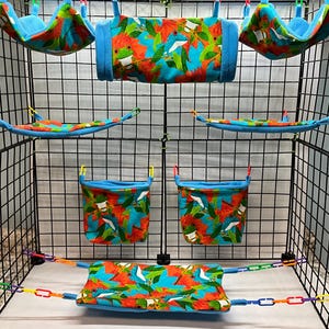 May include: A set of small animal cage accessories including two hanging hammocks, a cylindrical tunnel, two flat hammocks, two hanging pouches, and a rectangular mat. All items feature a vibrant tropical print with blue, orange, and green.