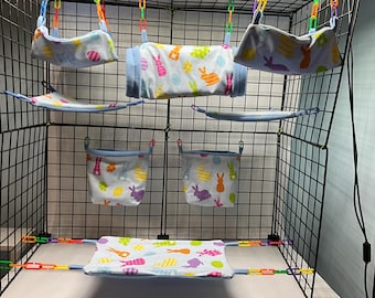 May include: A black wire cage with multiple hanging fabric hammocks and pouches for small animals. The fabric is blue with a white and colorful pattern of bunnies and eggs.