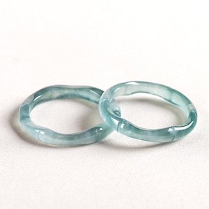 May include: Two jade green bangle bracelets, each with a slightly different shape, are arranged side by side on a white surface.