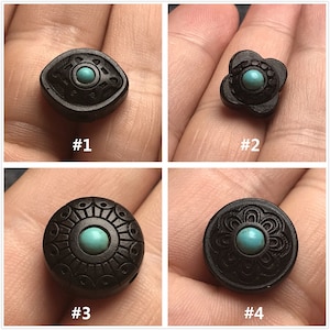 May include: Four black wooden beads with turquoise inlays. Each bead has a different design. #1 is an eye shape, #2 is a flower shape, #3 is a circle with a sunburst design, and #4 is a circle with a floral design.