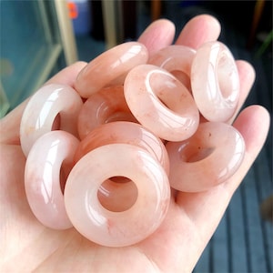 May include: A collection of eight pink and white donut-shaped crystal rings. The rings are made of polished stone and have a smooth, glossy finish.