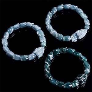 Puede incluir: Tres pulseras de jade en tonos azules y verdes se muestran sobre un fondo negro. Cada pulsera presenta un patr&oacute;n repetitivo de formas de animales talladas, con una talla de animal m&aacute;s grande como punto focal. Las pulseras son probablemente para usar en la mu&ntilde;eca.