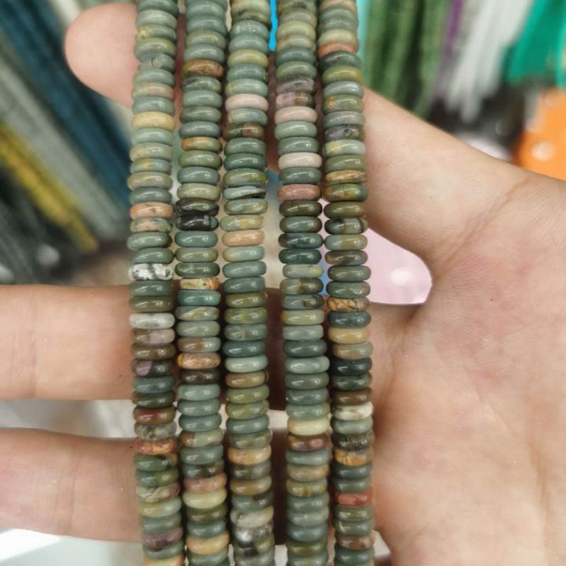 Pu&ograve; includere: Una collana di perline di pietre preziose multicolori. Le perline sono rotonde e hanno un motivo verde, marrone e bianco screziato. Le perline sono infilate su un filo trasparente.