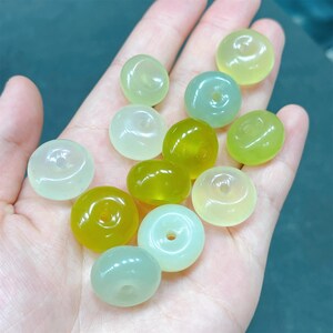 May include: A collection of round, green and white jade beads with a hole in the center. The beads are arranged in a hand.
