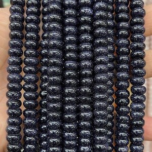 May include: A strand of dark blue gemstone beads with a sparkly, speckled finish. The beads are round and have a smooth, polished surface.