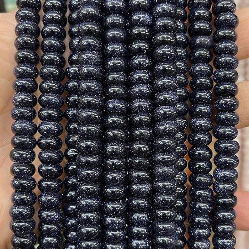 May include: A strand of dark blue gemstone beads with a sparkly, speckled finish. The beads are round and have a smooth, polished surface.
