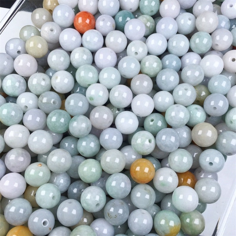 May include: A large collection of round, smooth, light green jade beads. The beads are various shades of green, white, and light brown.