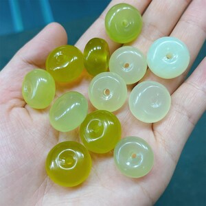 May include: A collection of green and yellow jade beads with a hole in the center. The beads are smooth and polished.