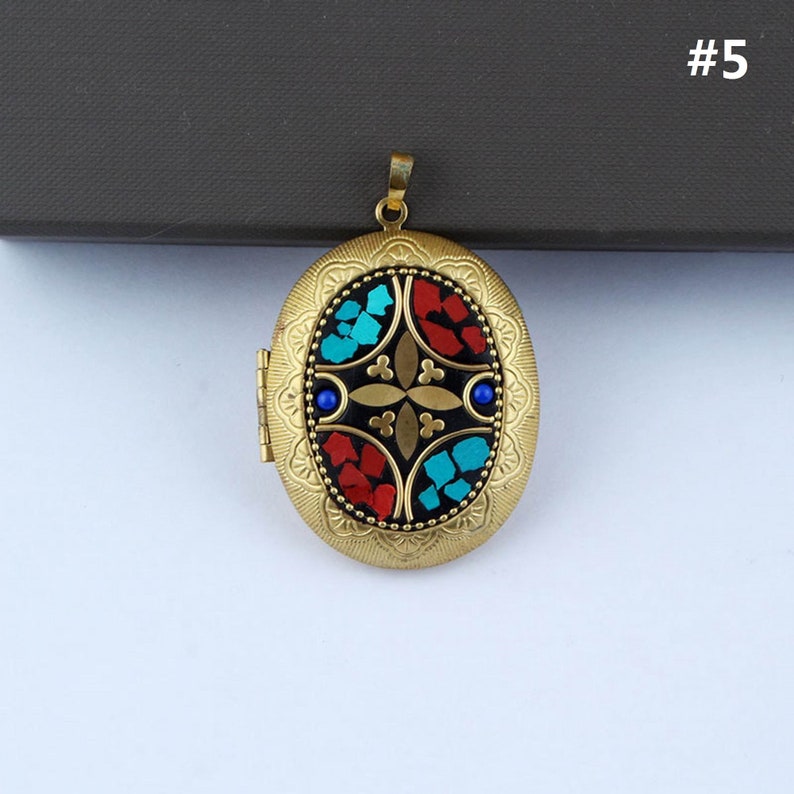 May include: Gold oval locket with a black background and a colorful mosaic design. The mosaic features red, blue, and turquoise pieces arranged in a geometric pattern.
